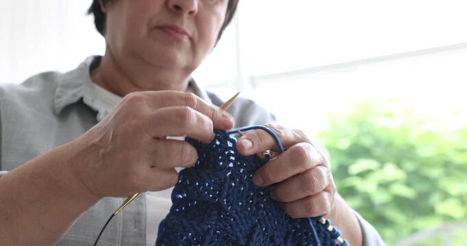 Senior woman knitting with needles indoors, closeup