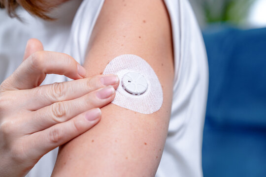 Person pressing a white circular glucose monitor sensor firmly onto a bare shoulder area while preparing for daily glucose tracking