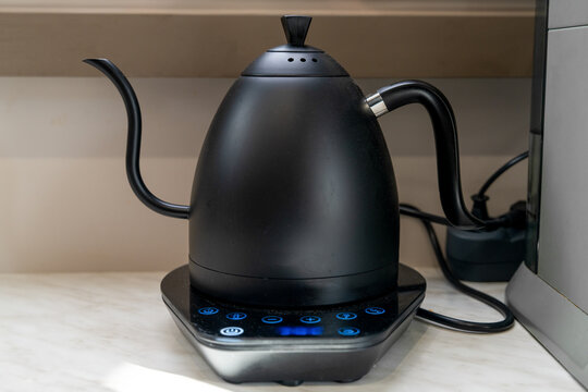 Sleek black gooseneck electric kettle with a slender spout standing on a marble counter in a minimalist modern kitchen interior