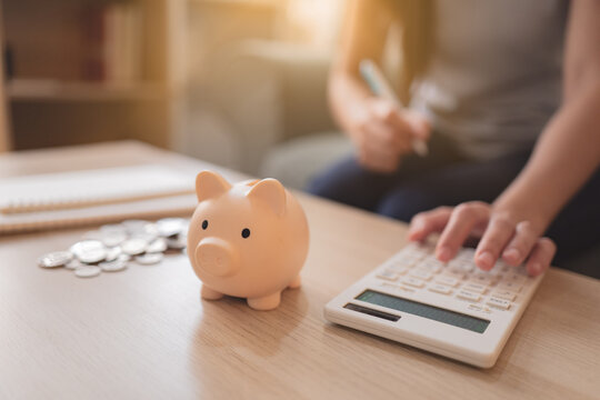 Person using a calculator beside a piggy bank and coins at home, representing personal finance, household budgeting, expense calculation, savings planning, and smart money management