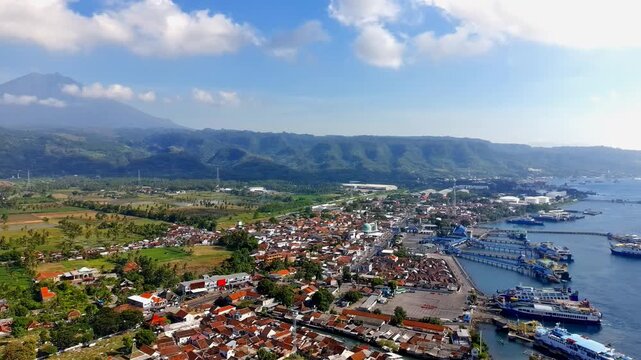 Aerial view of Ketapang Ferry Port with docked ships and surrounding coastal town buildings under a blue sky in Kalipuro, East Java, Indonesia.