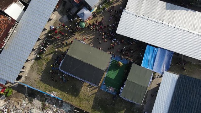 Aerial footage of a crowd of residents watching a traditional dance, amidst the density of an urban village, Yogyakarta, Indonesia.