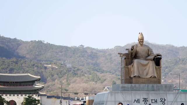 A bronze seated statue of King Sejong the Great in front of Gyeongbokgung Palace with mountains visible in the background in Seoul.