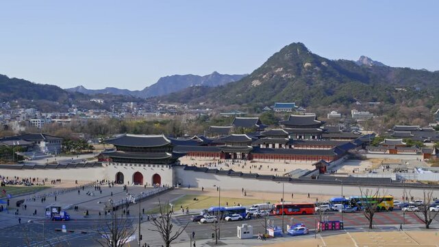 A wide view of Gwanghwamun Plaza with the gate visible in the background and mountains behind it under a clear sky.