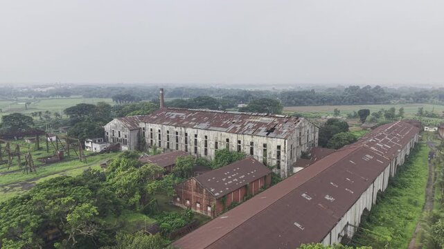 Drone footage flying forward toward Kushtia Sugar Mill, capturing factory buildings, industrial infrastructure, production facilities, and the surrounding manufacturing area in daylight.