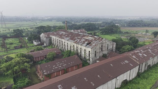 Drone footage circling Kushtia Sugar Mill in a semi-orbit movement, revealing factory buildings, industrial infrastructure, production facilities, and the surrounding landscape in daylight.