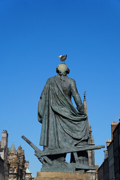 Statue of philosopher Adam Smith featuring a plough and a resting seagull resting on a historical statue in Edinburgh Old Town