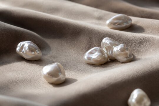 Irregular pearl nodules scattered on velvet fabric in close-up with soft texture and shallow depth.