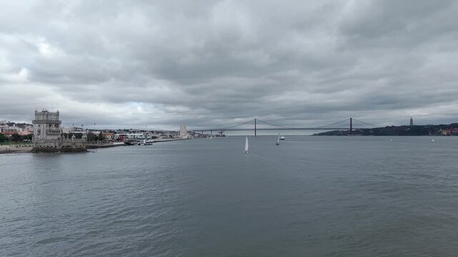 Sailboats on Tagus River harbour, Belem Tower and Ponte 25 de Abril bridge in background under an overcast sky, Lisbon, Aerial view
