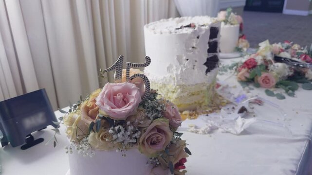 Close-up of a decorated quincea&ntilde;era cake featuring floral arrangements and a "15" topper as guests serve slices during a celebration. The scene captures a traditional Sweet 15 reception with cake cutt
