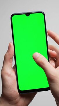 Person holding smartphone with green screen performing zoom gesture on neutral background