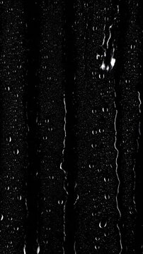 Rain drops sliding down glass surface against black background in a seamless loop