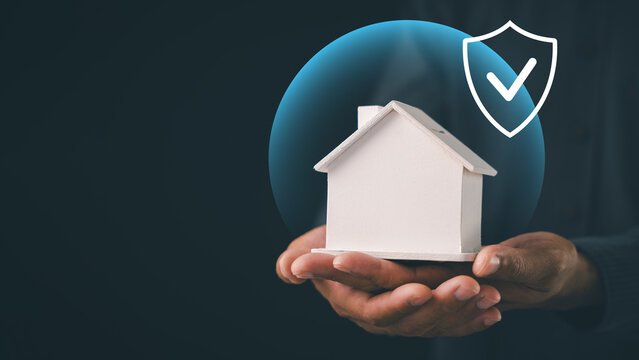 Home insurance and property protection concept shown with hands holding miniature house model under safe glowing shield, securing housing coverage and mortgage against financial risk