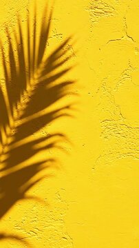 Shadow of a palm leaf swaying on a bright yellow textured wall with copy space for text