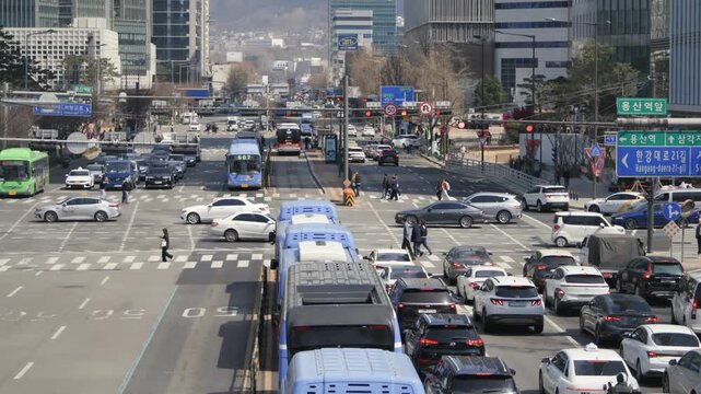 A wide aerial-style view of a congested road in downtown Seoul with multiple lanes of vehicles and urban buildings.