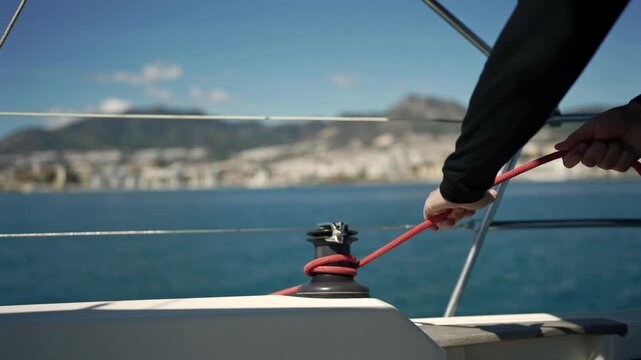 Sailor's hands pulling a red rope on a yacht winch