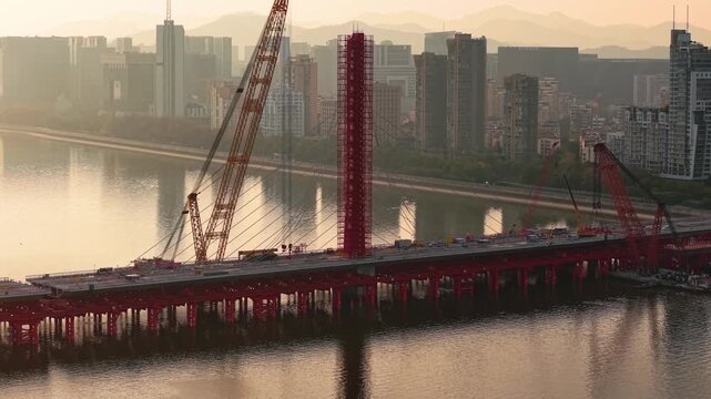 Aerial view of bridge demolition in China, cable-stayed structure being dismantled with cranes over river on the sunset