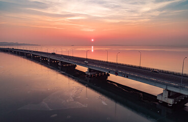 Aerial drone view of low-water bridge across the bay with moving car during the sunset. Active movement of transport cars vehicles in different directions. © Evgenii Bakhchev