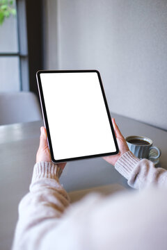 Vertical mockup image of a woman holding digital tablet with blank white desktop screen in cafe