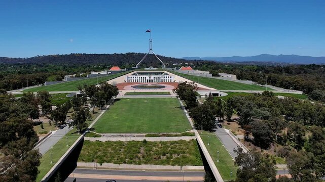 Aerial view of Parliament House with its iconic flagpole, expansive green lawns, and surrounding gardens in Canberra, Australian Capital Territory, Australia.