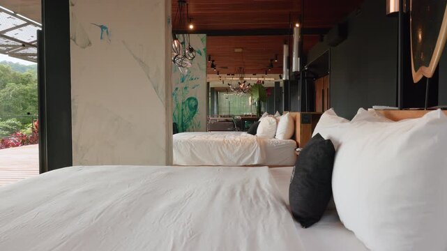 Luxurious boutique hotel suite featuring two beds with white linens and decorative pillows. Wooden ceiling and artistic hummingbird murals complement the open-air design with jungle views.