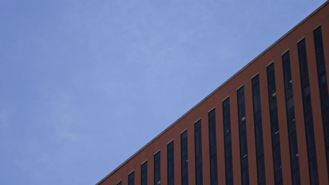 A low angle abstract view of a modern red brick building corner with clean geometric lines against a bright blue sky.