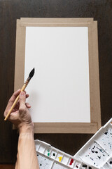 Left Handed Artist Using a Professional Squirrel Hair Mop Brush to Paint on Stretched White Paper Mounted on a Wooden Board in a vertical composition
