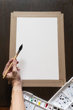 Left Handed Artist Using a Professional Squirrel Hair Mop Brush to Paint on Stretched White Paper Mounted on a Wooden Board in a vertical composition