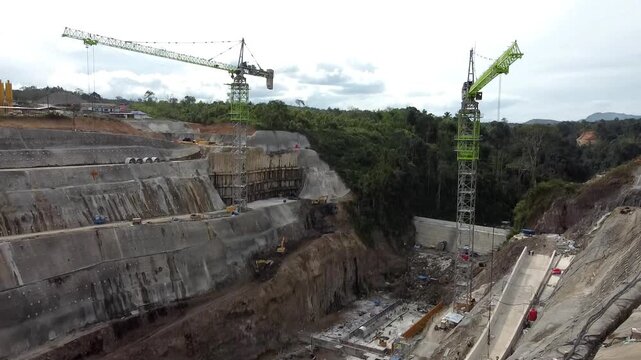 Aerial view of the PLTA Kerinci Merangin Hidro construction site with heavy machinery, concrete structures, and excavation works in Batang Merangin, Jambi, Indonesia.