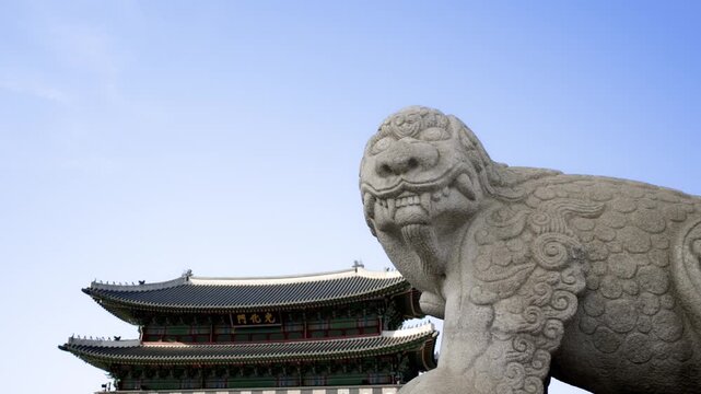 A side view of a stone Haechi guardian statue with Gwanghwamun Gate visible in the background on a clear day.