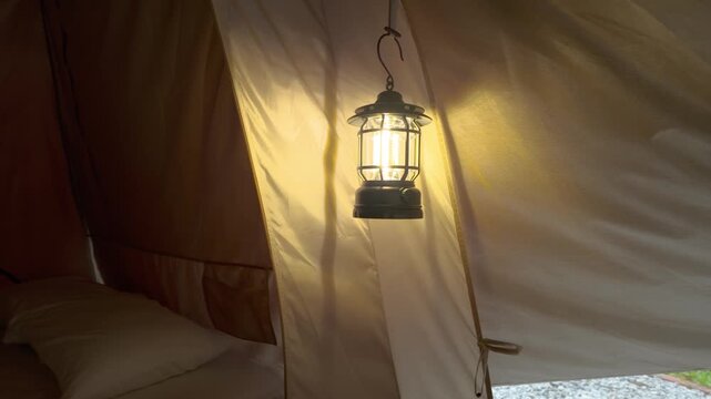 Warm LED camping lantern hanging inside a cozy canvas tent, casting a soft glow over the sleeping area to create a comfortable and inviting glamping atmosphere.