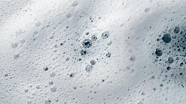Top-down macro of dense washing foam surface with bubbles forming circular patterns and gently bursting. Subtle rotation emphasizes texture, cleanliness, and dynamic micro activity in a fresh setting