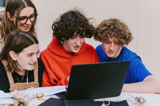 Diverse group of teenage students collaborating around a laptop for education and teamwork imagery, featuring soft matte textures and overcast light