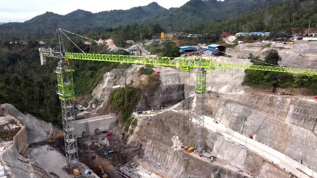 Aerial view of the PLTA Kerinci Merangin Hidro construction site with large tower cranes, concrete structures, and excavation work in Batang Merangin, Jambi, Indonesia.