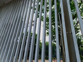 Obraz premium Looking up through white vertical concrete fence bars with green trees backdrop