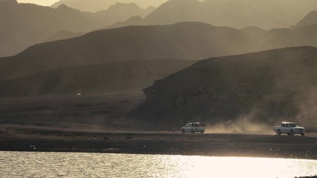 Distant view of Pickup Truck driving Near Coastal Mountains at sunset and blowing dust