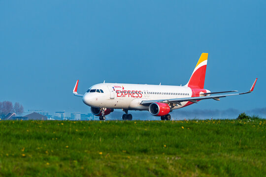 Amsterdam, Netherlands, 21.04.2023 - An Iberia Express passenger airliner taxiing on the runway at Schiphol Airport during a clear spring day with green grass in foreground.