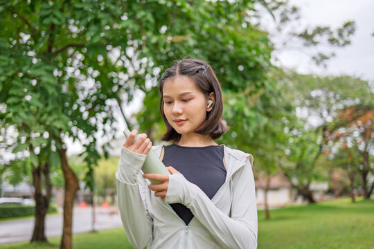 Asian Gen Z woman using reusable stainless tumbler after jogging in green urban park for sustainable wellness lifestyle