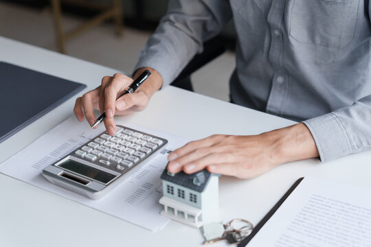 Asian businessman pressing calculator with touching house model real estate investment concept