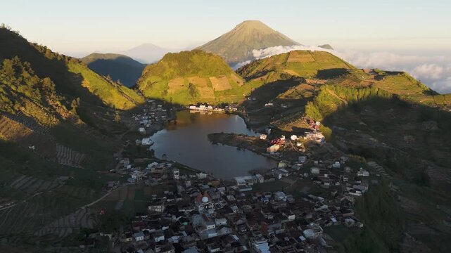 Aerial view of Telaga Cebong lake nestled among the volcanic mountains and terraced fields of the Dieng Plateau in Indonesia.