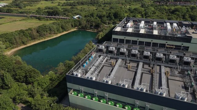 Aerial view of a modern data center facility featuring rooftop cooling units and industrial infrastructure situated next to a pond and green space in London, London, United Kingdom.