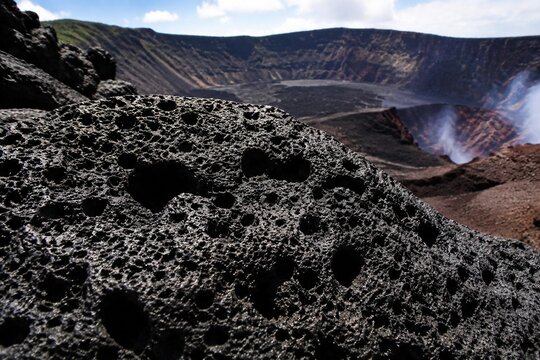 Porous black volcanic scoria at a crater's edge, textured surface.