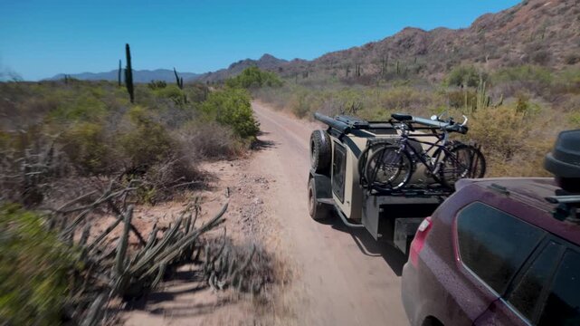 SUV moves along sandy road in desert while pulling a teardrop camper trailer through Baja California in Mexico.