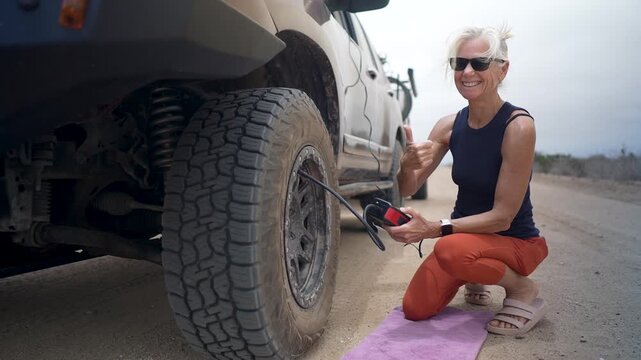 Senior woman smiles as she inflates the tires of her suv and teardrop camper after an adventure in baja california Mexico desert
