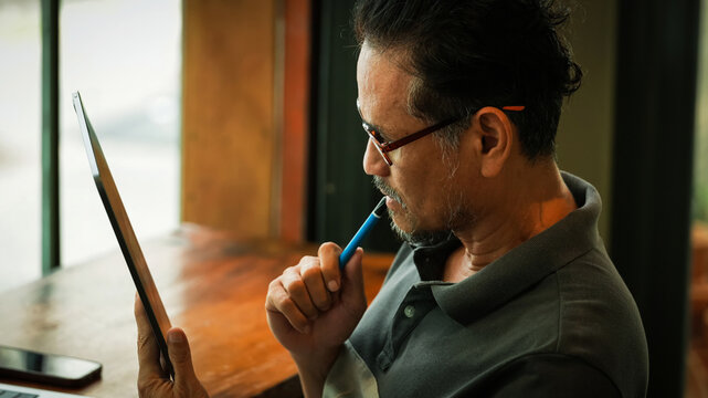 Senior executive reviewing information on a digital tablet while thinking in a modern workspace. Concept of business analysis