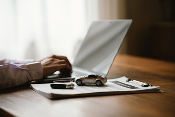 Fototapeta premium Person holding a model car beside a laptop, symbolizing vehicle insurance, auto finance, online car valuation, and ownership.
