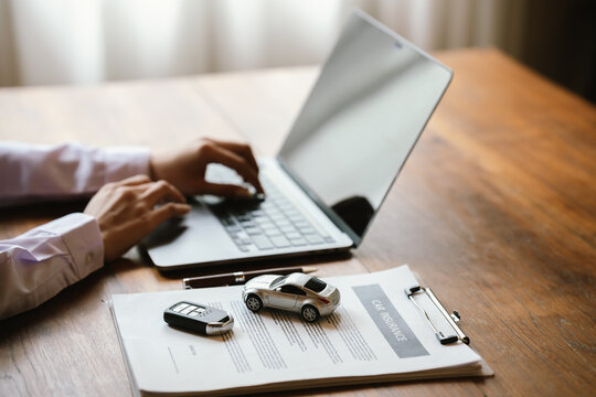 Person holding a model car beside a laptop, symbolizing vehicle insurance, auto finance, online car valuation, and ownership.
