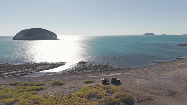 Suv parked with teardrop camper trailer on the beach at sunrise. Family enjoys an overland adventure in Baja California Mexico.