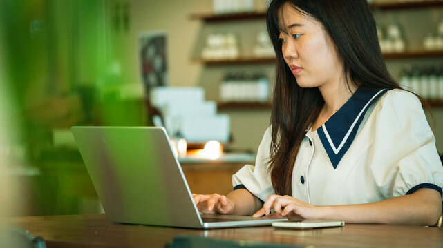 Focused Young Asian Businesswoman Working on Laptop at Modern Coffee Shop