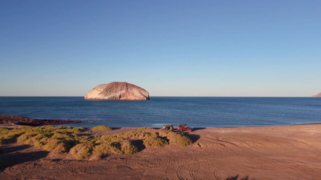 Two travelers set up camp by the beach at sunset using an suv and a teardrop camper in Baja California Mexico.